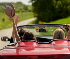 Four people in a red convertible car. Each of them has one arm in the air. One is holding a straw hat. They embody the joy of a soul connection.