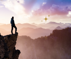 Person standing on the edge of a cliff looking into the distant mountains where they can see gold stars that represent their potential future when they learn how manifestation works.