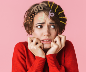 A woman has her hands up to her chin and a very worried look on her face. There are squiggles across her brown and in her hair to illustrate mental activity. She is not confidant in her self-expression.