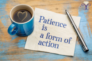 A blue mug with a heart shape in the surface of the drink sits slightly on top of a napkin. The napkin is white with blue writing that reads 'patience is a form of action'. There is a pen sitting across the top right hand corner of the napkin.